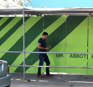 Person texting beside striped green fence