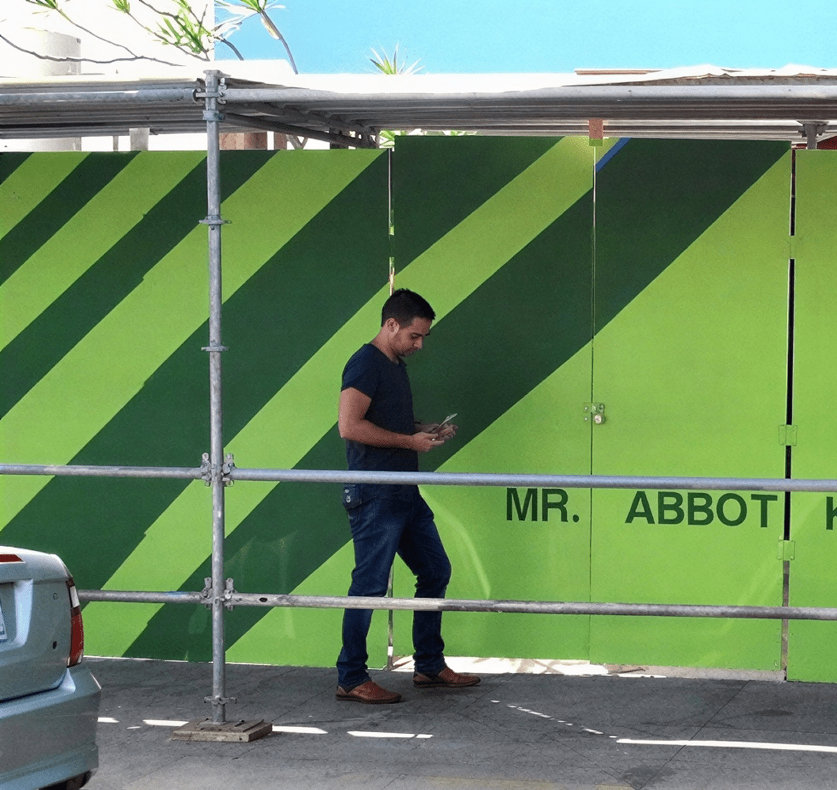Person texting beside striped green fence