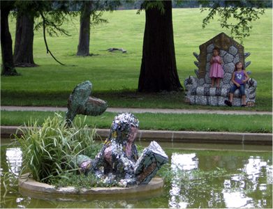 Garden sculptures near pond and trees.