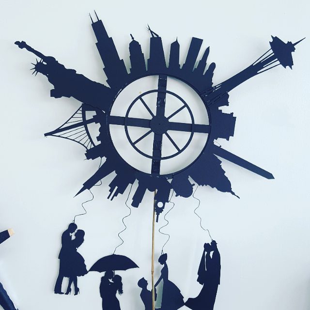 Silhouette art with cityscape and people figures.