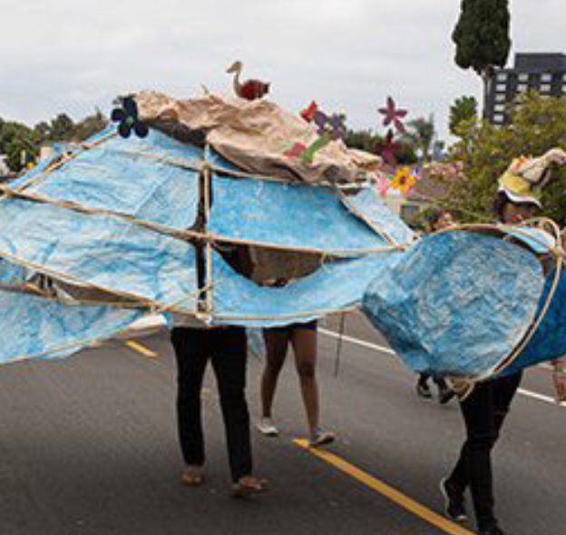 People carrying large blue paper mache structure.
