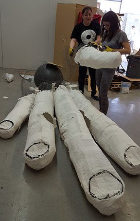 Two people constructing large paper mache octopus.