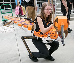 Person wearing an orange dinosaur costume outdoors.