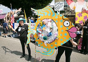 People with fish-shaped trash display at parade.