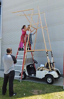 People assembling wooden structure on ladders.