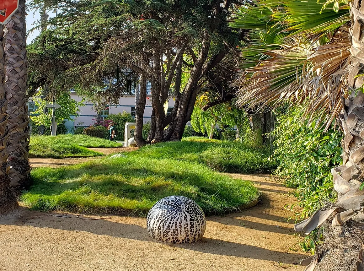 Garden path with trees and decorative sphere.