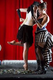 Two performers onstage with red curtain backdrop.