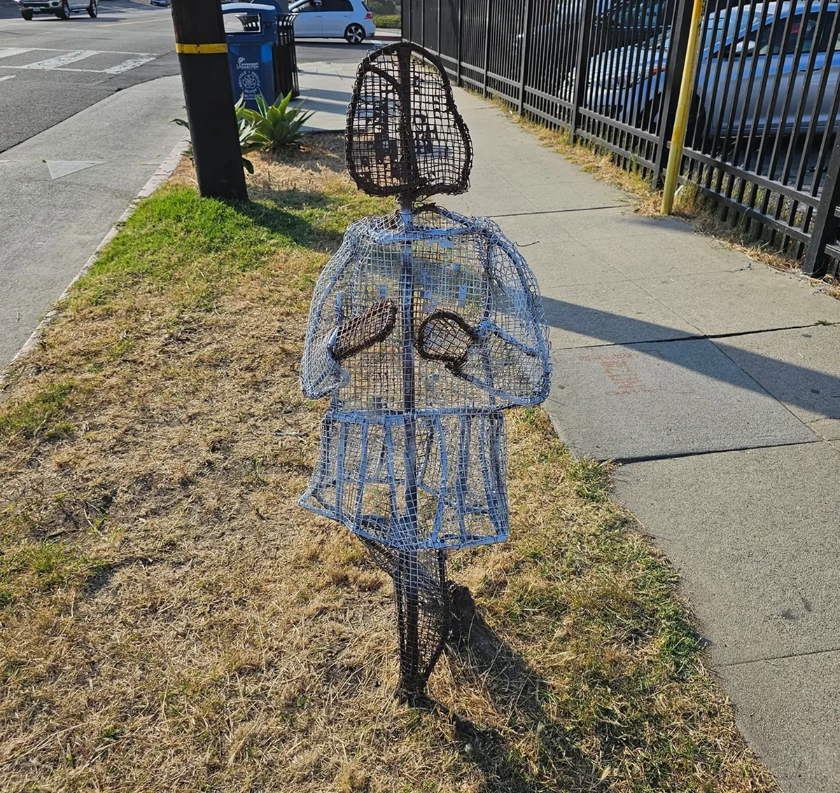 Wire sculpture of a person on sidewalk.