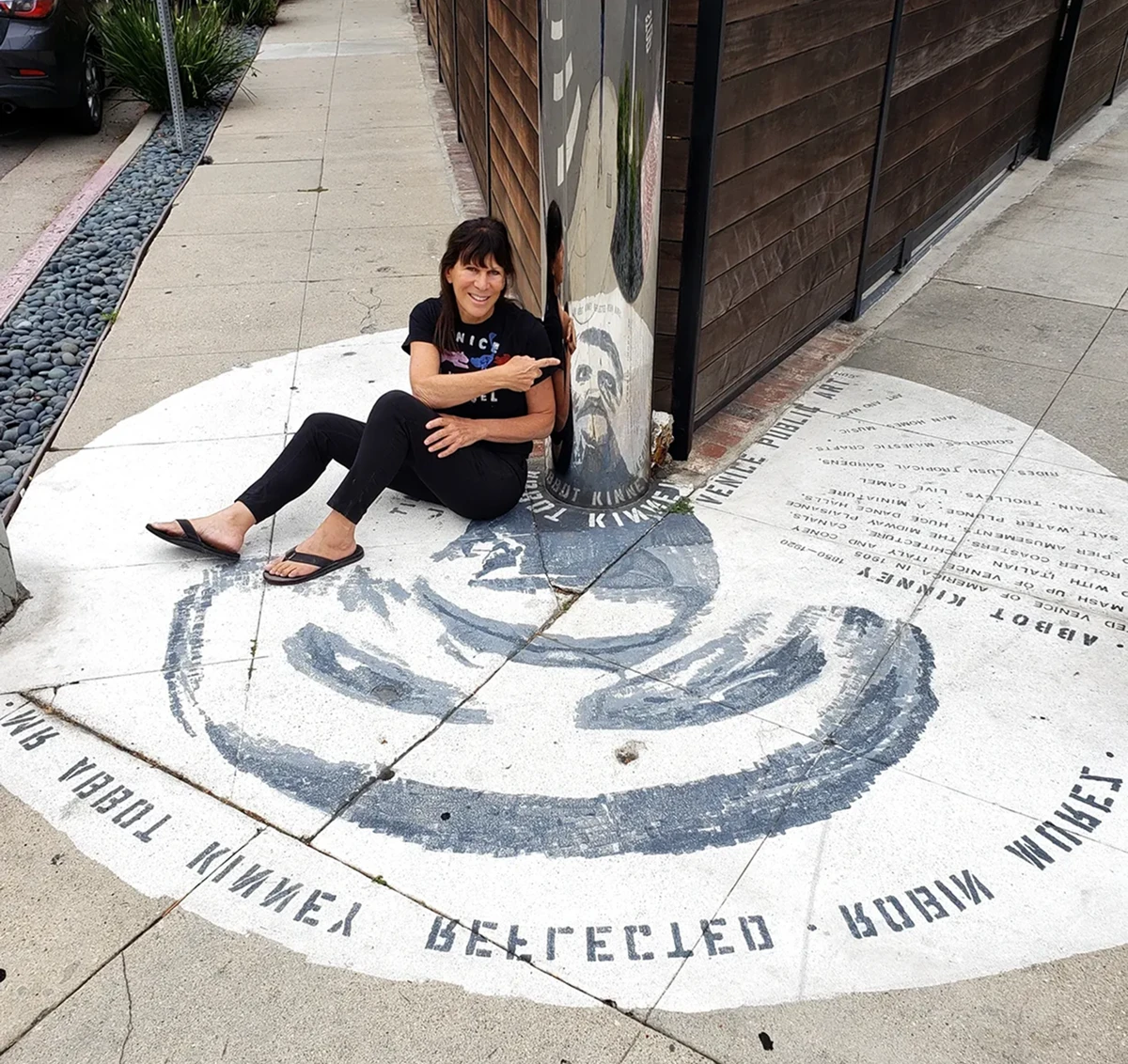 Woman sitting beside mirrored column artwork.