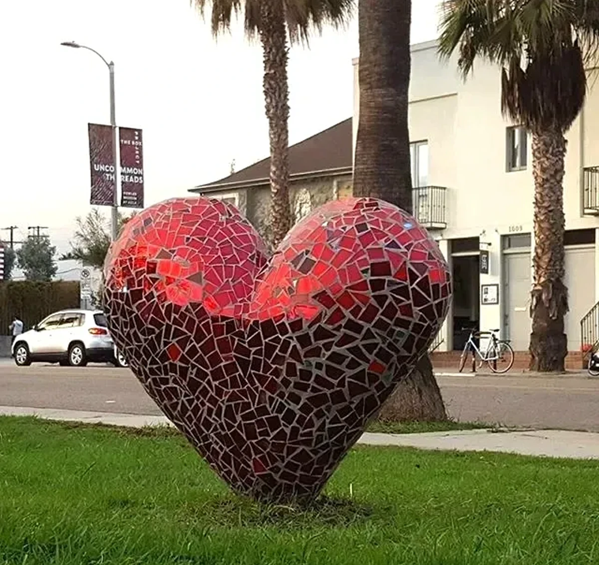 Mosaic heart sculpture on urban grass field.