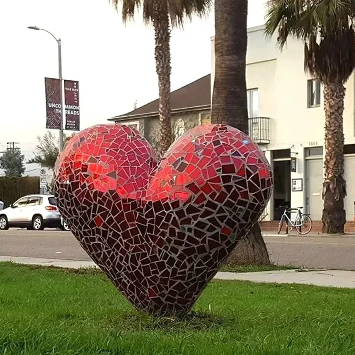 Mosaic heart sculpture on urban grass field.