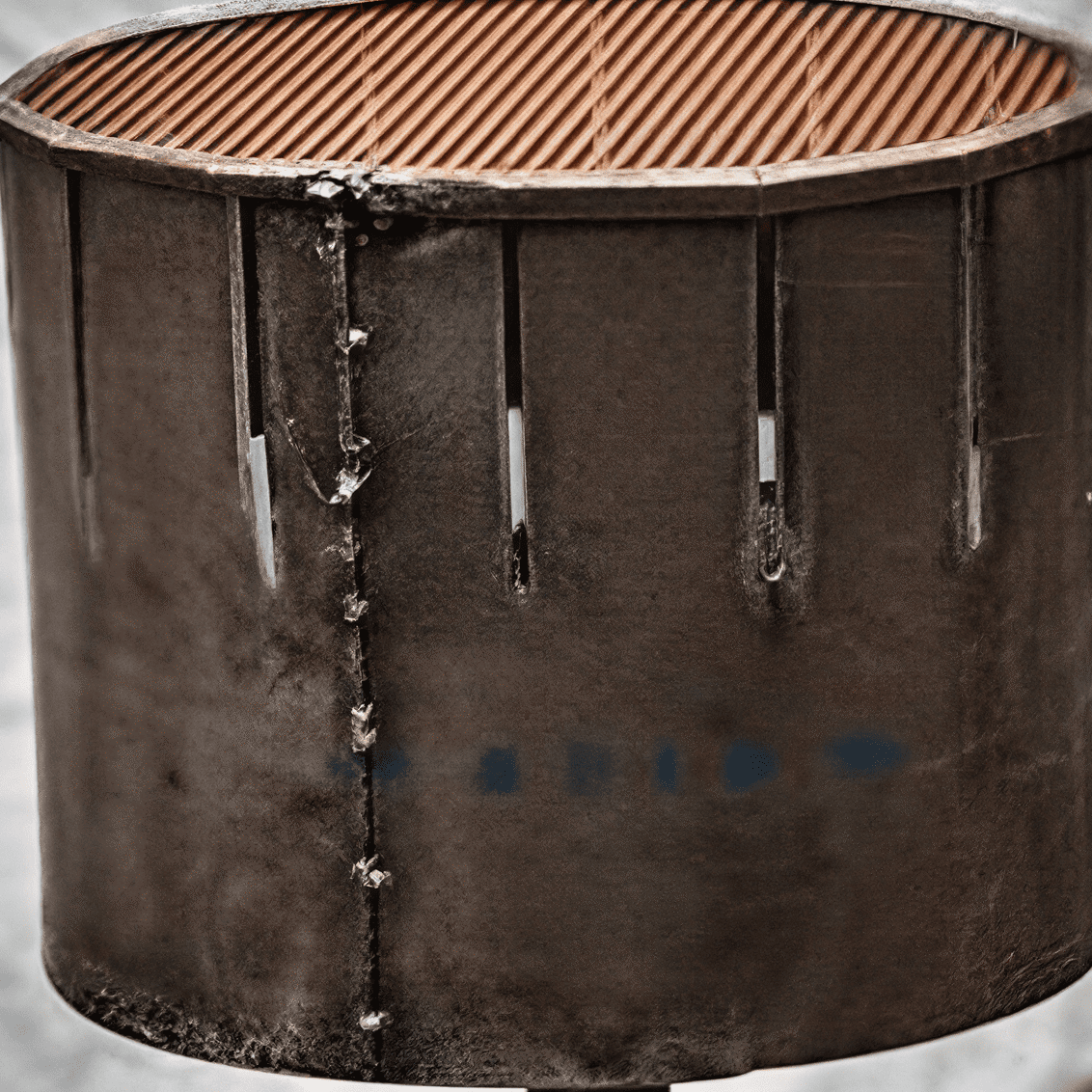 Rusty metal barrel with vertical slits.